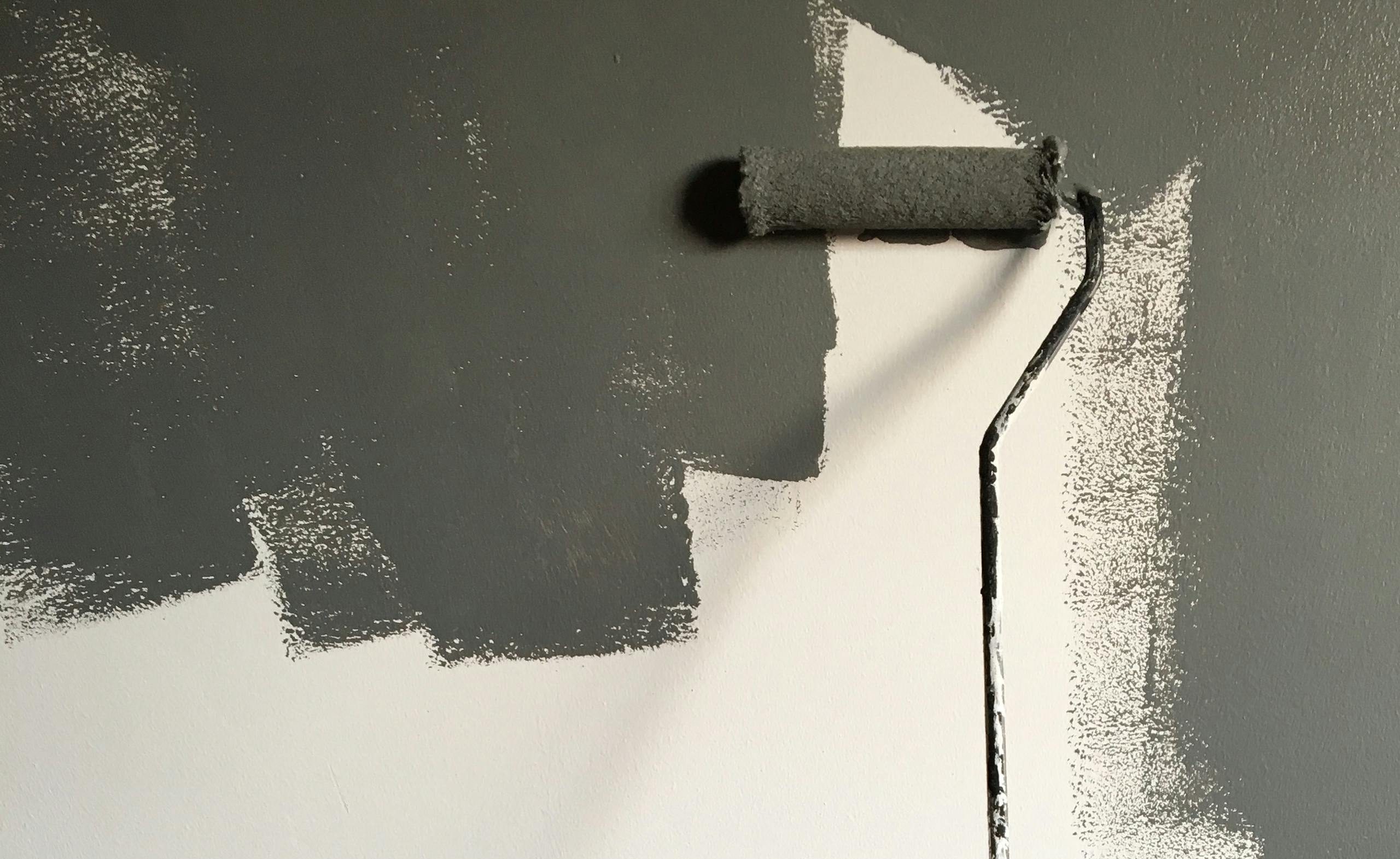 A hand painting a wall gray with a roller during a house renovation project.