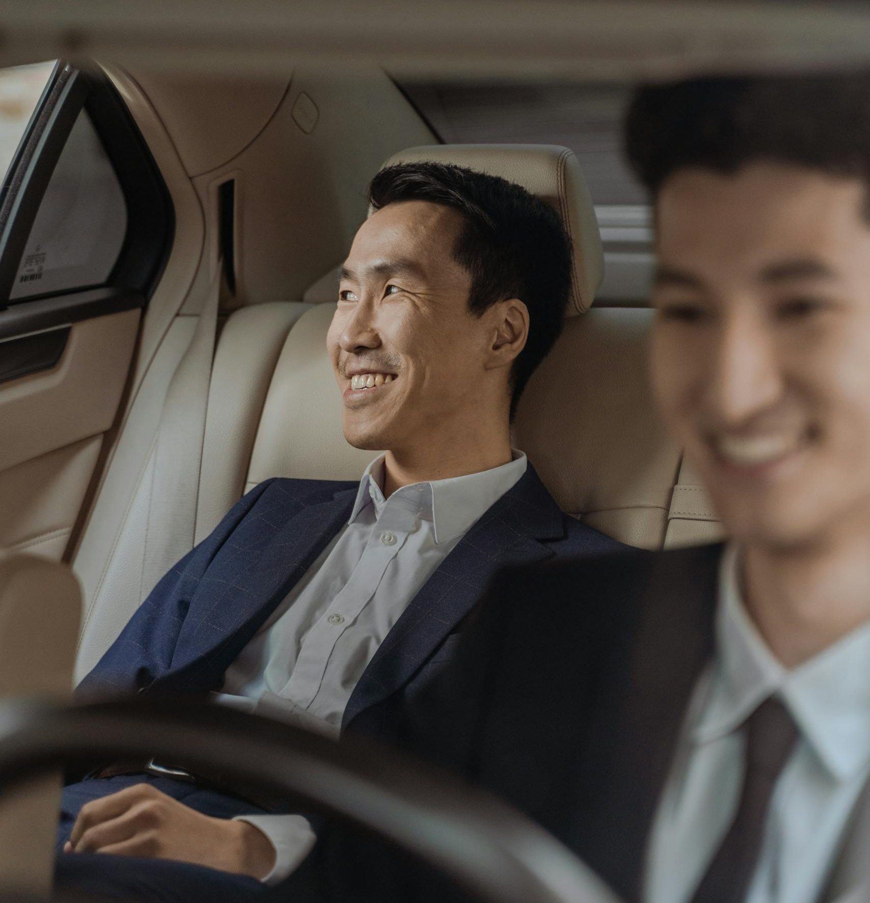 Two men in formalwear enjoying a comfortable ride in a luxury car, smiling.
